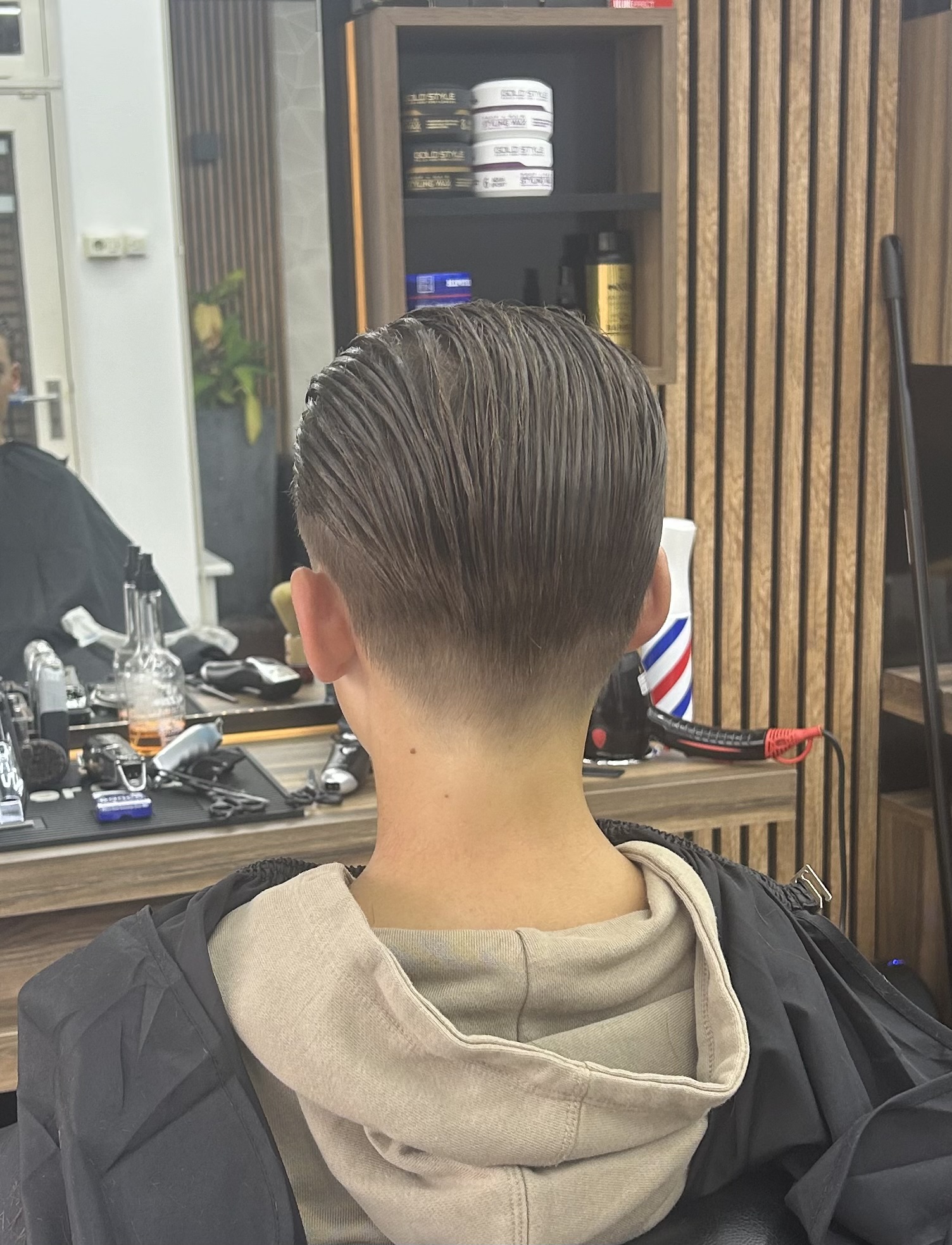 Een afgewerkt kapsel van achteren gezien, met de barberspaal op de achtergrond